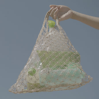 A hand holding a bag of plastic bottles picked up from the beach.